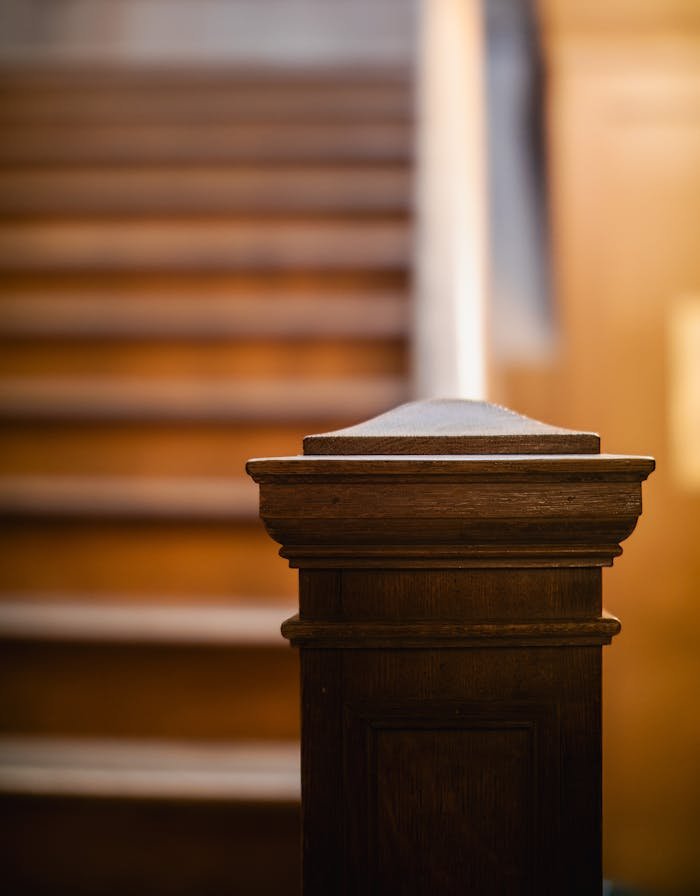 Detailed view of a wooden staircase post in a warmly lit interior setting.